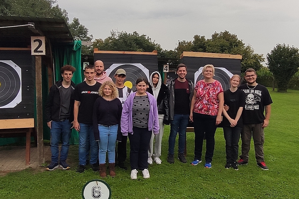 Azubis und Bildungsbegleiter stehen vor großen Zielscheiben am Bogenschießplatz in Aislingen